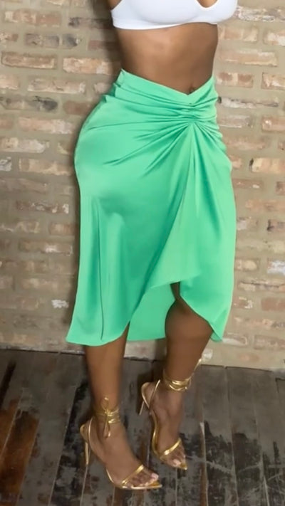 Person wearing a green skirt and white top against a brick wall.