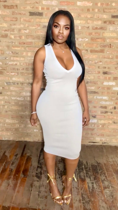 Woman wearing a white dress against a brick wall.